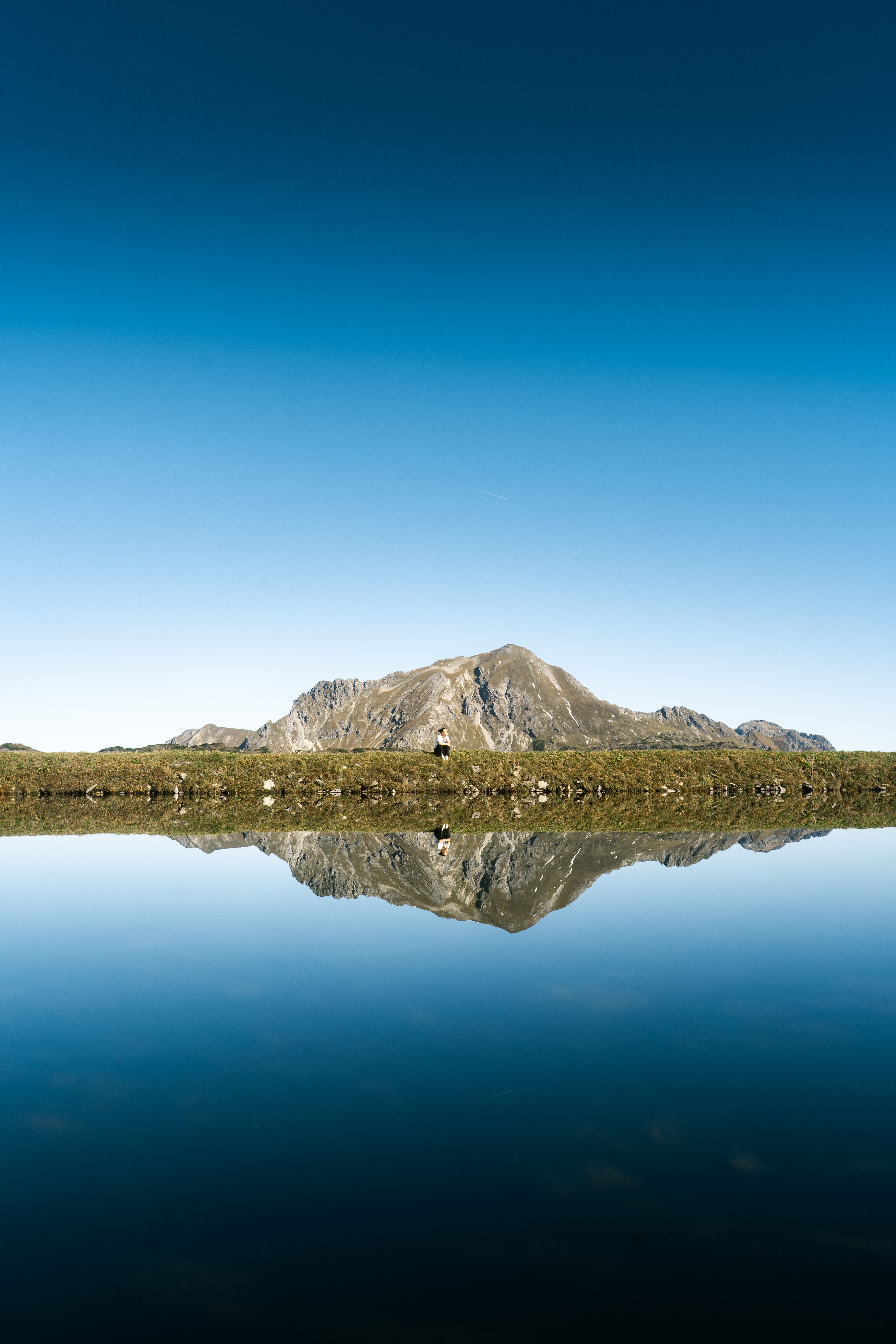 Calm alpine lake reflects majestic mountain under clear blue sky, ideal for relaxing or nature wanderlust.