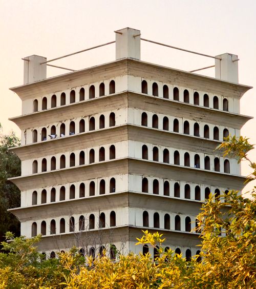 Free A multi-story birdhouse with numerous arched openings, set in a park with surrounding greenery. Stock Photo