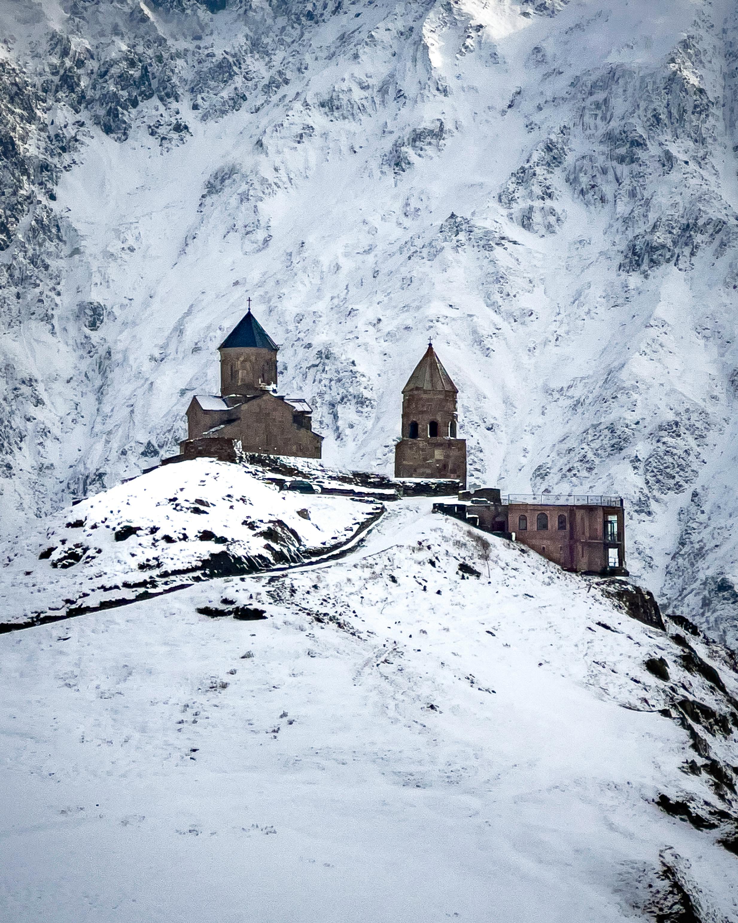 Scenic view of Gergeti Trinity Church covered in snow against towering mountains.