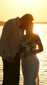 A couple embraces during a sunset wedding by a serene lake, capturing a moment of love.
