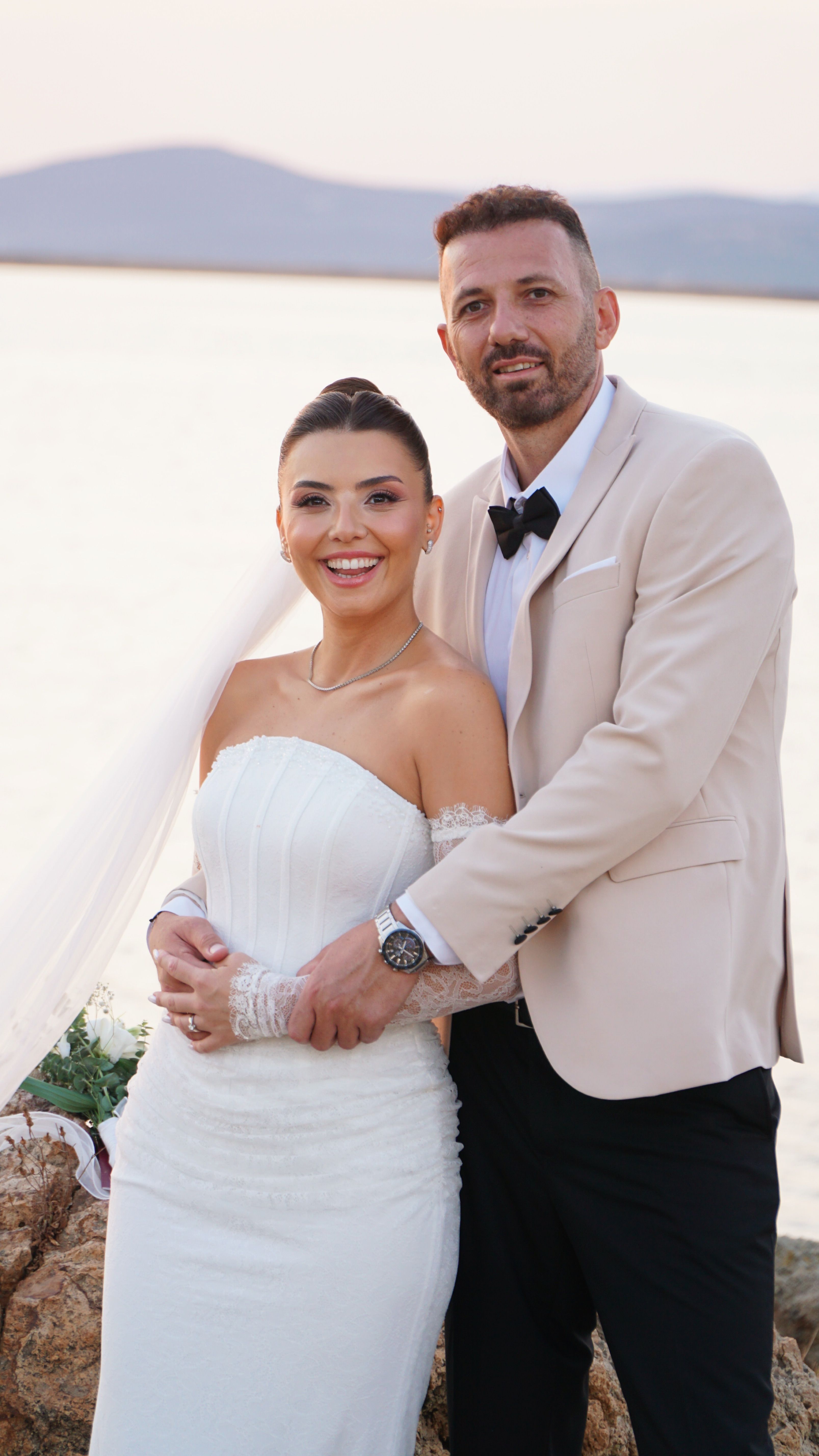 Newlyweds pose by the sea during a beautiful sunset, capturing a memorable wedding moment.