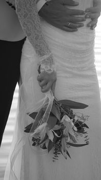 Close-up of a bride and groom holding a bouquet on their wedding day in black and white.