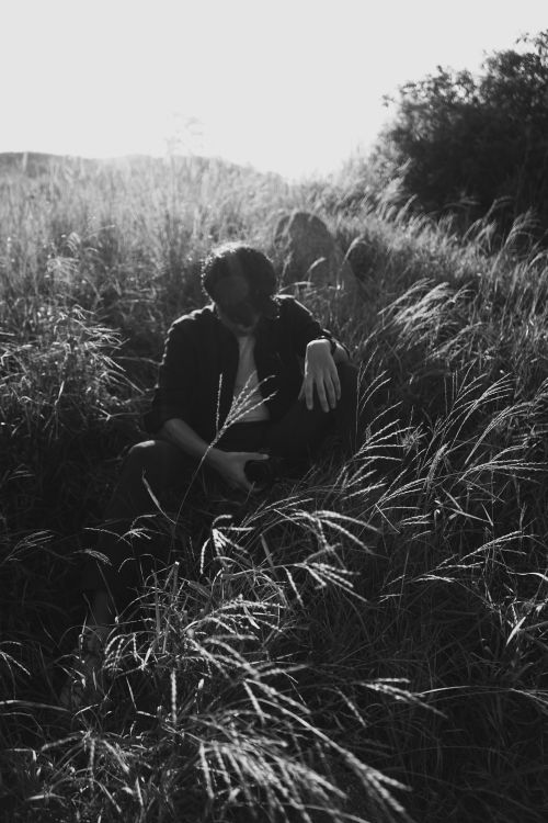 Free Black and white photo of a person sitting among tall grass, evoking a sense of solitude and reflection. Stock Photo
