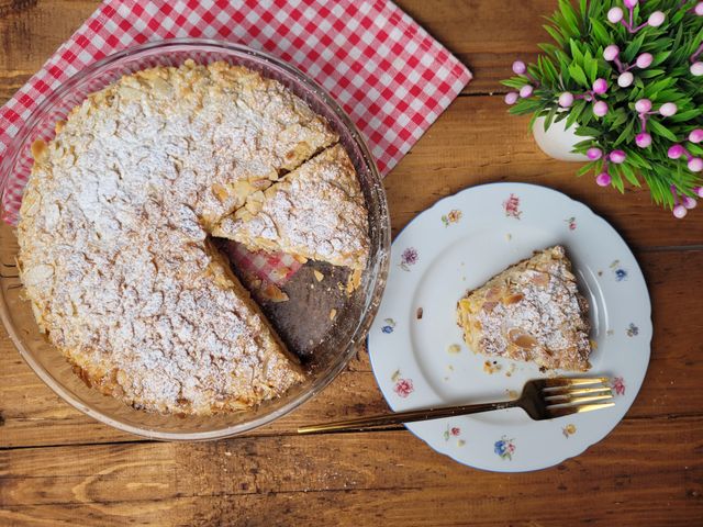 Delicious homemade almond cake with powdered sugar and a slice served on a rustic table setting.