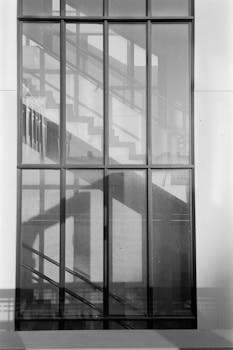 Black and white image capturing staircase reflections through glass, creating a pattern.