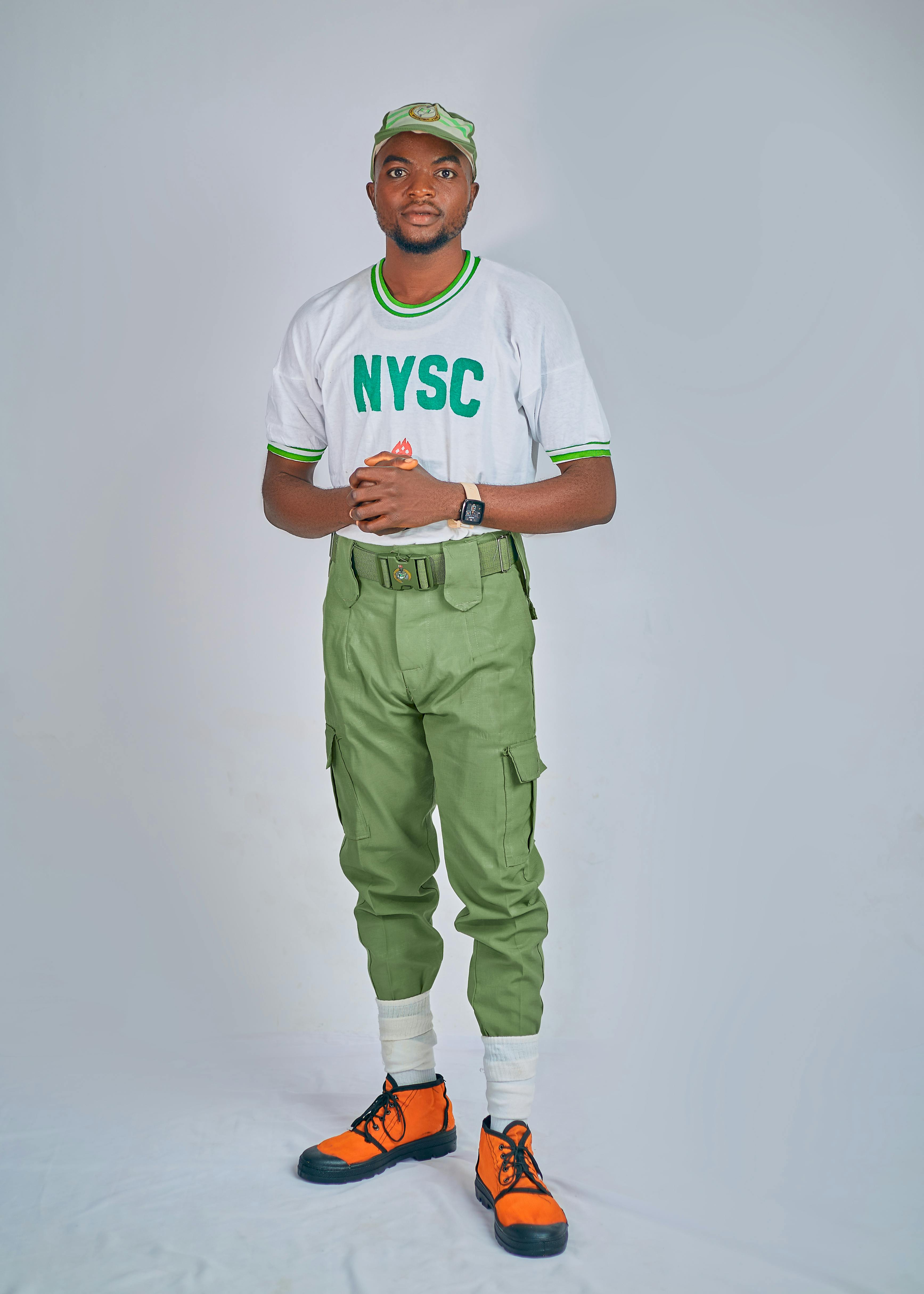 Young man in NYSC uniform standing confidently against a plain background.