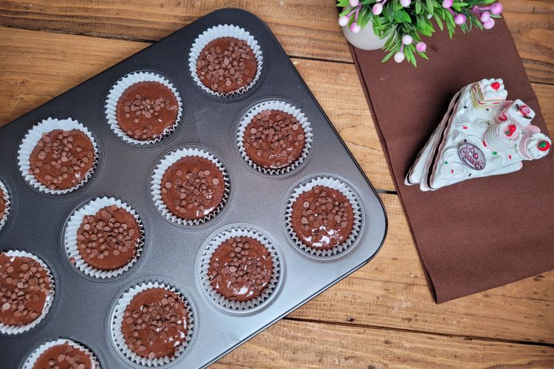 Freshly baked chocolate chip muffins in a tray with decorative plates nearby on a wooden table.