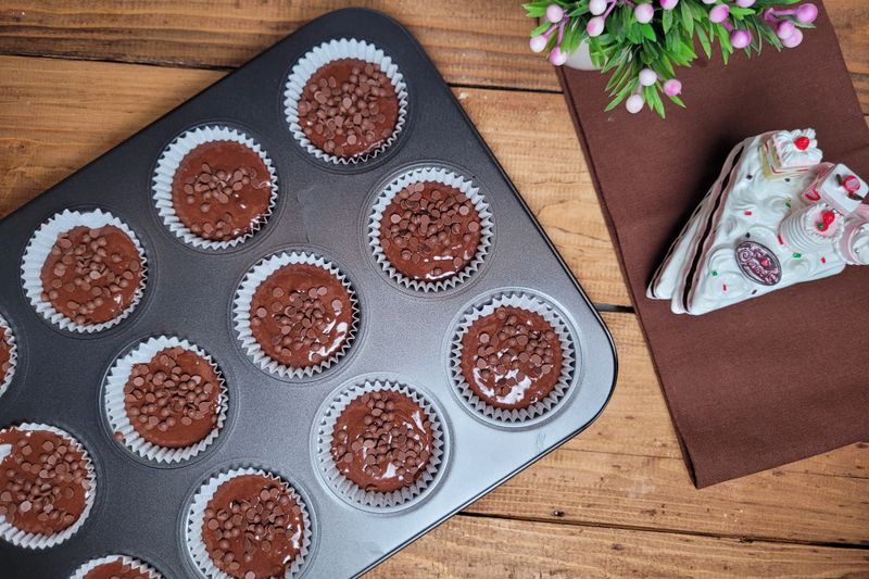 Freshly baked chocolate cupcakes with choco chips on a rustic wooden table.