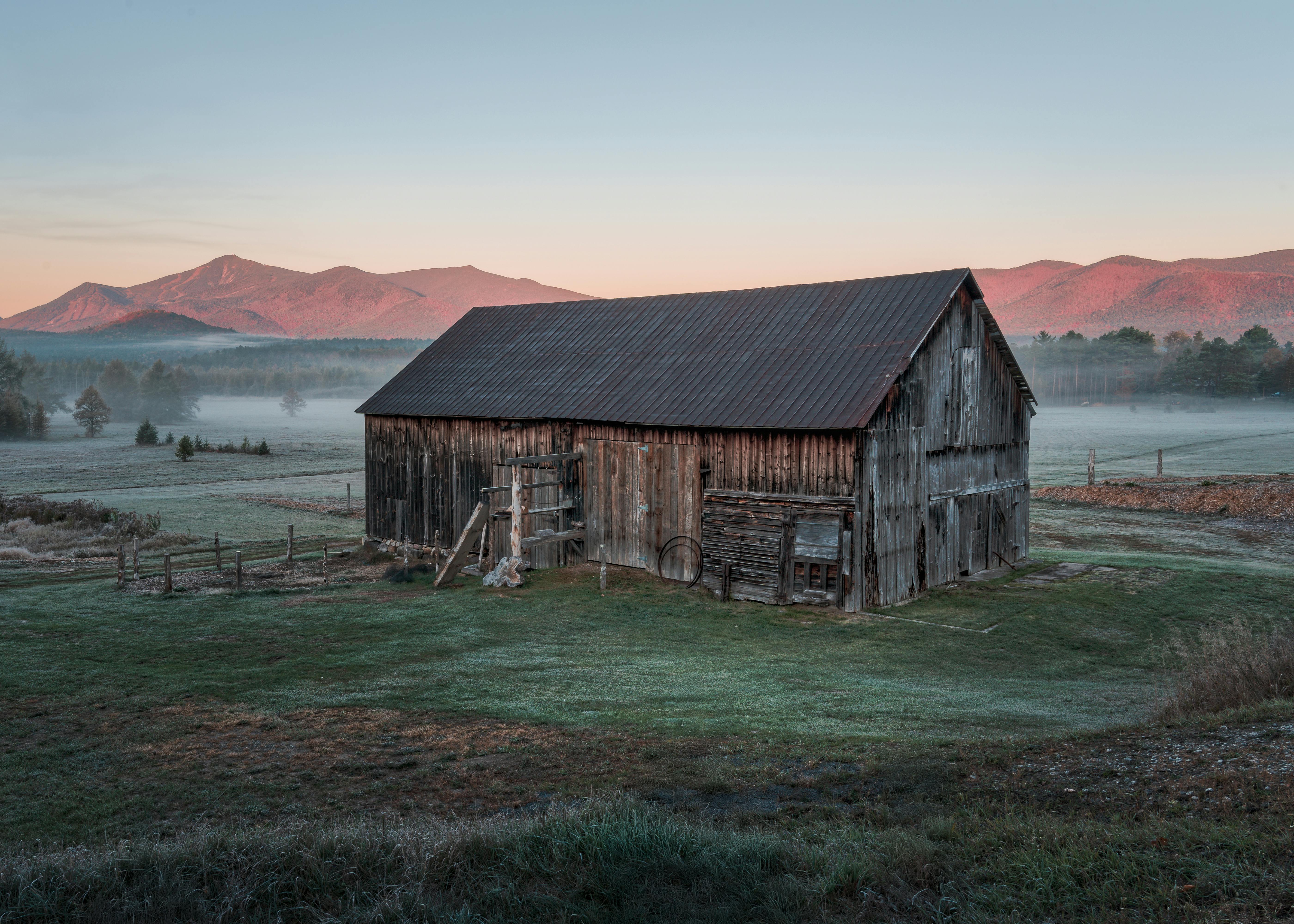 A vintage barn set against the misty Adirondack mountains at sunrise in Wilmington, New York.