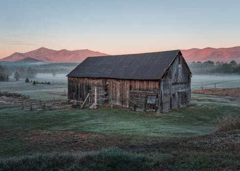 A vintage barn set against the misty Adirondack mountains at sunrise in Wilmington, New York.