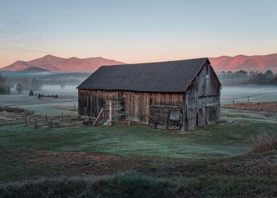 A vintage barn set against the misty Adirondack mountains at sunrise in Wilmington, New York.