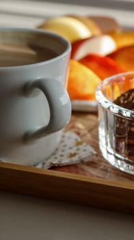 Warm morning setup with coffee, sliced fruit, and treats on a wooden tray.