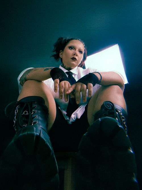 Free Edgy portrait of a woman in alternative fashion with combat boots and a tie, studio setting. Stock Photo