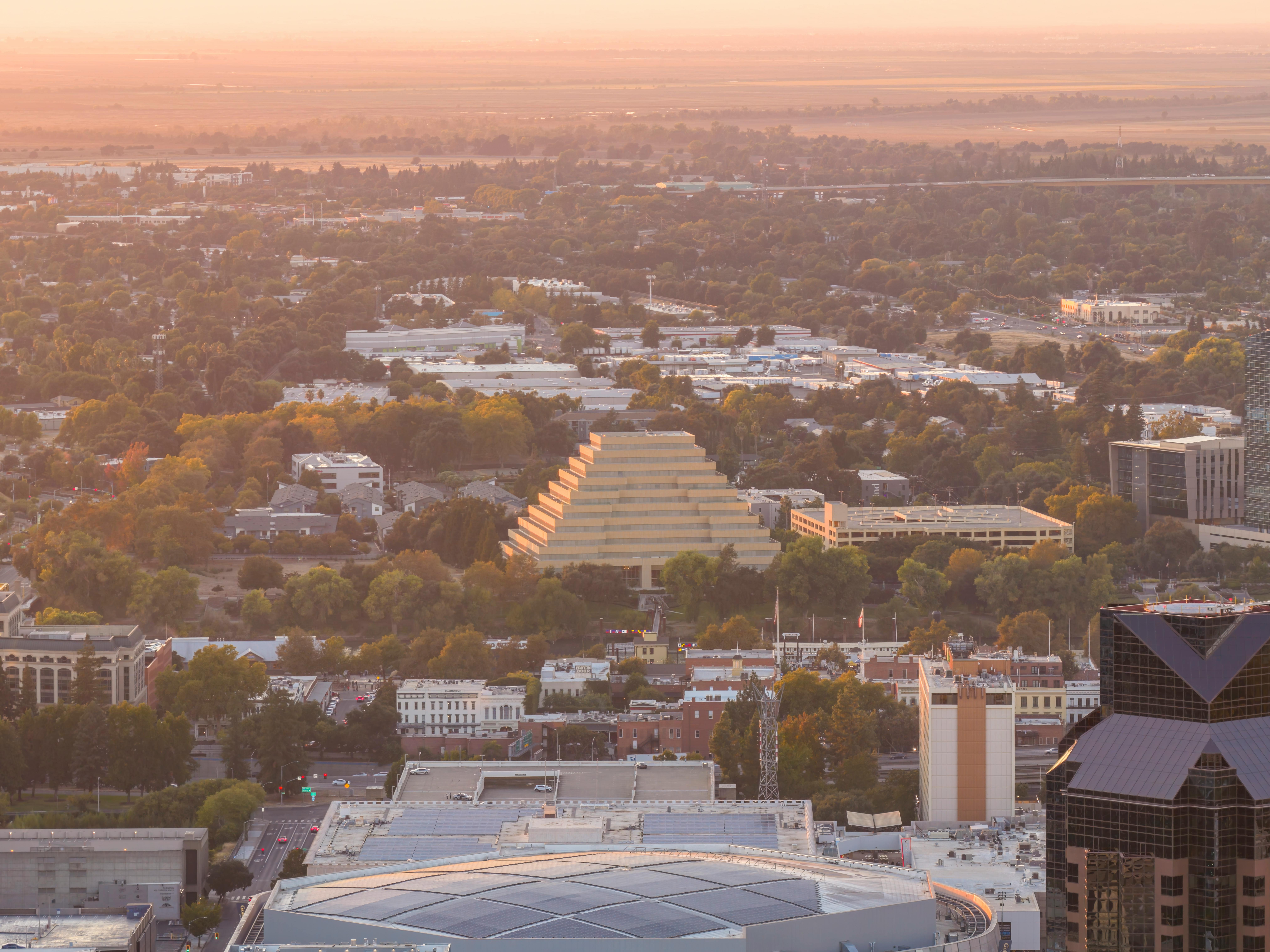 grátis Vista aérea do horizonte de Sacramento ao pôr do sol, destacando o icônico edifício piramidal e a vegetação exuberante. Foto profissional