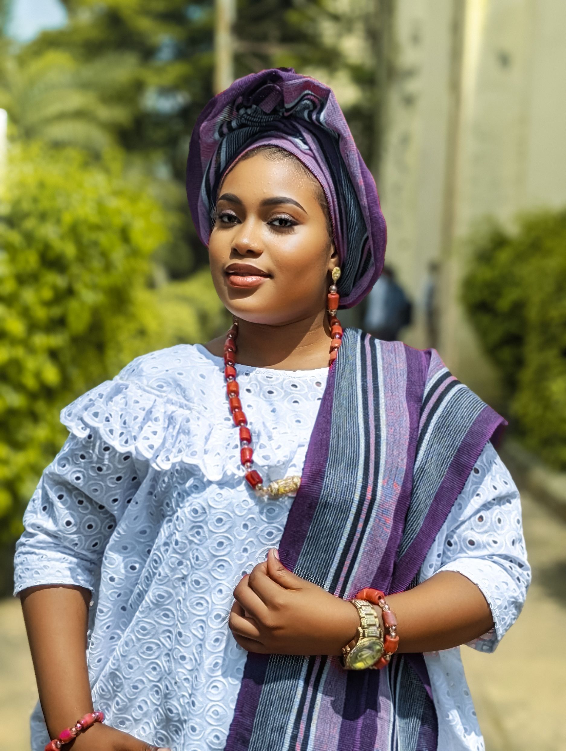 Elegant African woman wearing traditional clothing and accessories, smiling confidently outdoors.