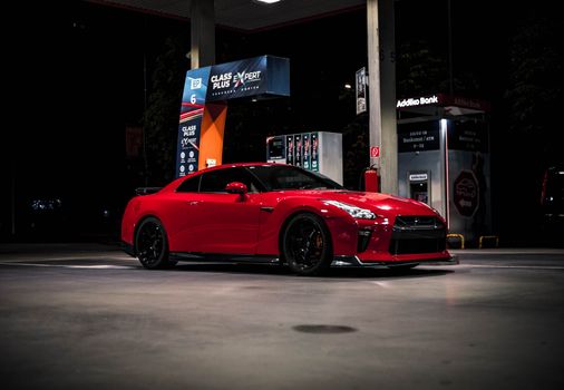 Red Nissan GTR parked at a gas station in Sarajevo during nighttime, showcasing its sporty design.