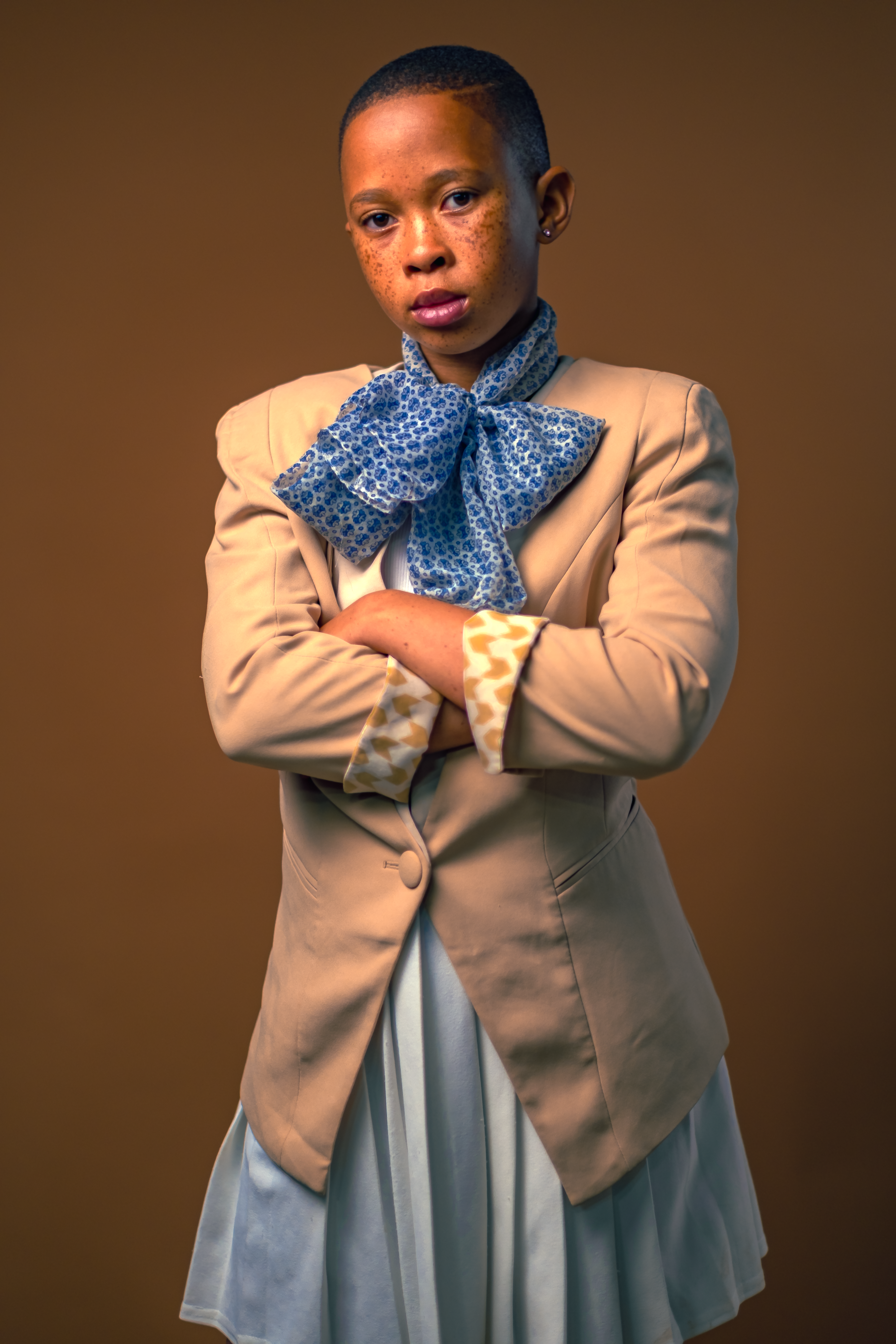 Portrait of a stylish young teen with folded arms and a cool expression in a neutral setting.