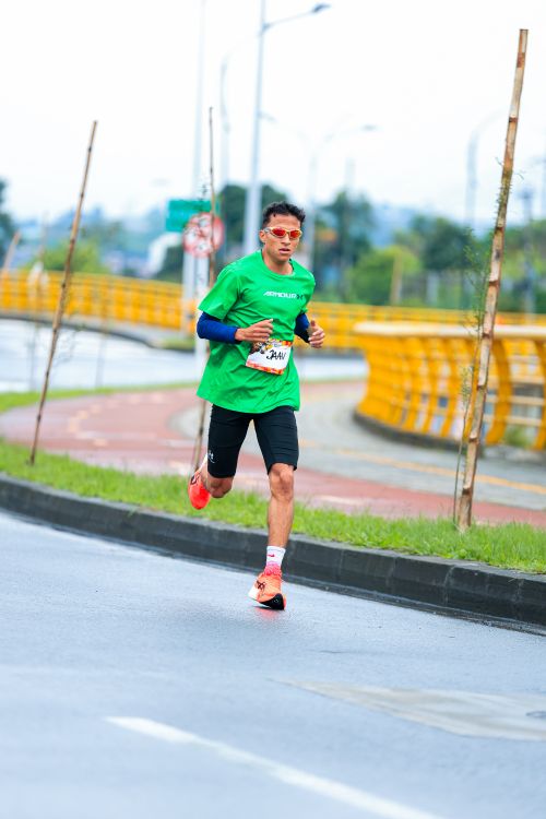 Free Male runner wearing green shirt competing in outdoor marathon on city road. Stock Photo