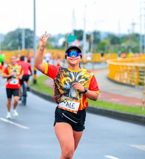 Free Female marathon runner in vibrant attire showing peace sign on road. Energetic and determined. Stock Photo