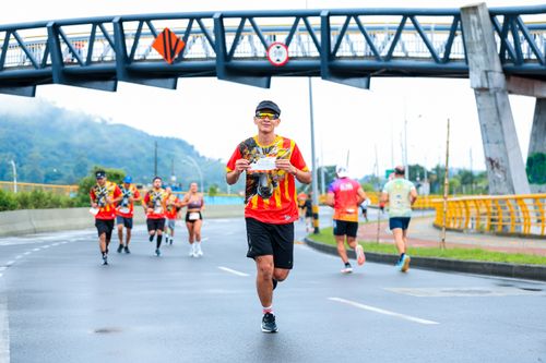 Free Marathon runners in colorful shirts race under a bridge on a city street. Stock Photo