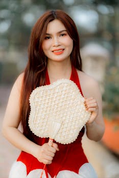 Portrait of a woman in a red dress holding a traditional woven fan outdoors.