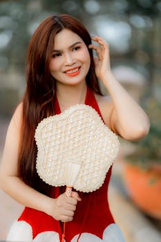 Beautiful woman with long hair and red dress holding a woven fan.