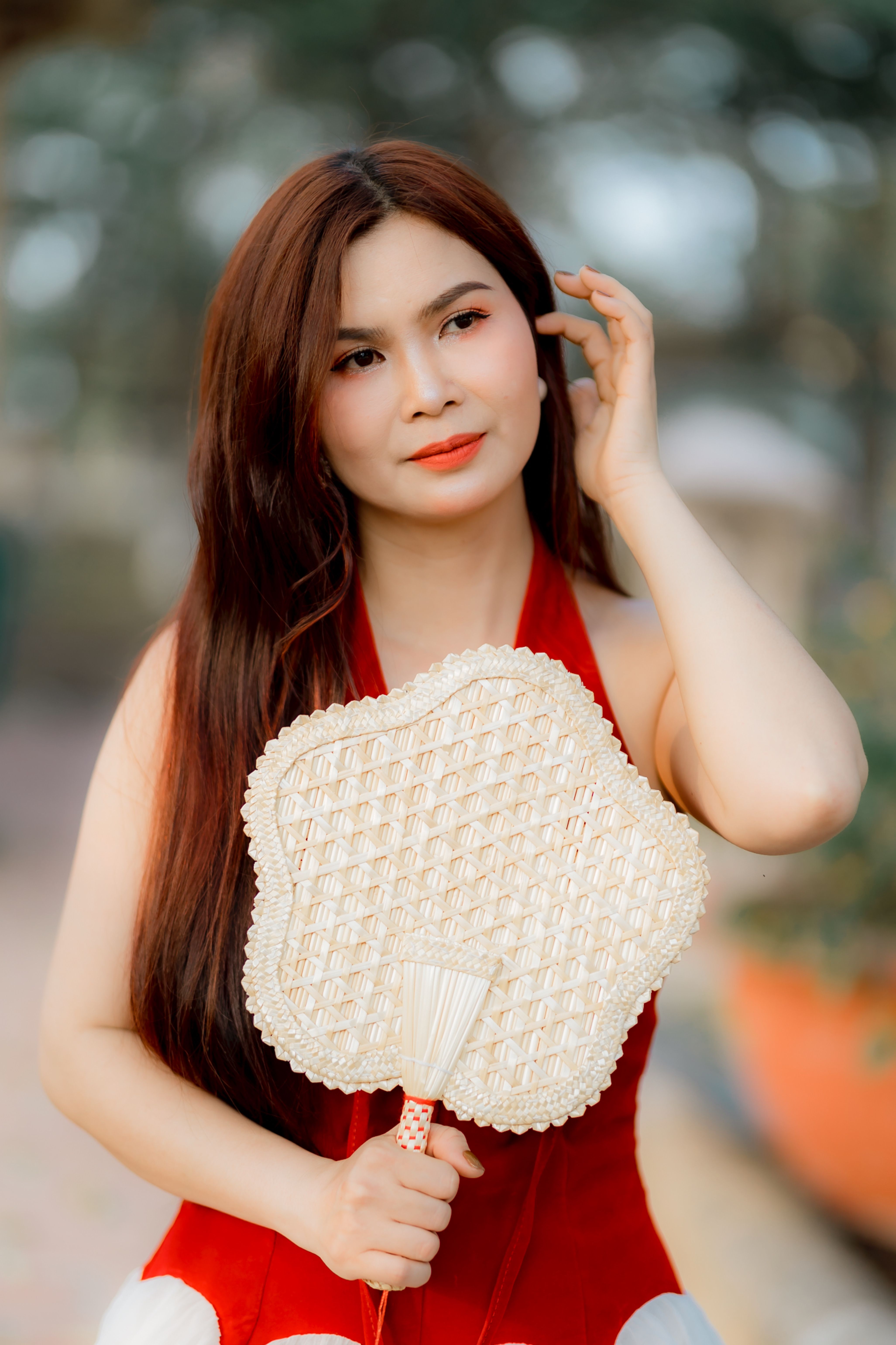 Portrait of a woman holding an intricately crafted fan in a serene outdoor setting.