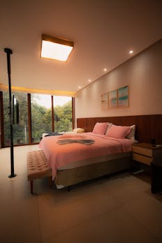 Elegant modern bedroom with pink decor and a scenic forest view through large windows.