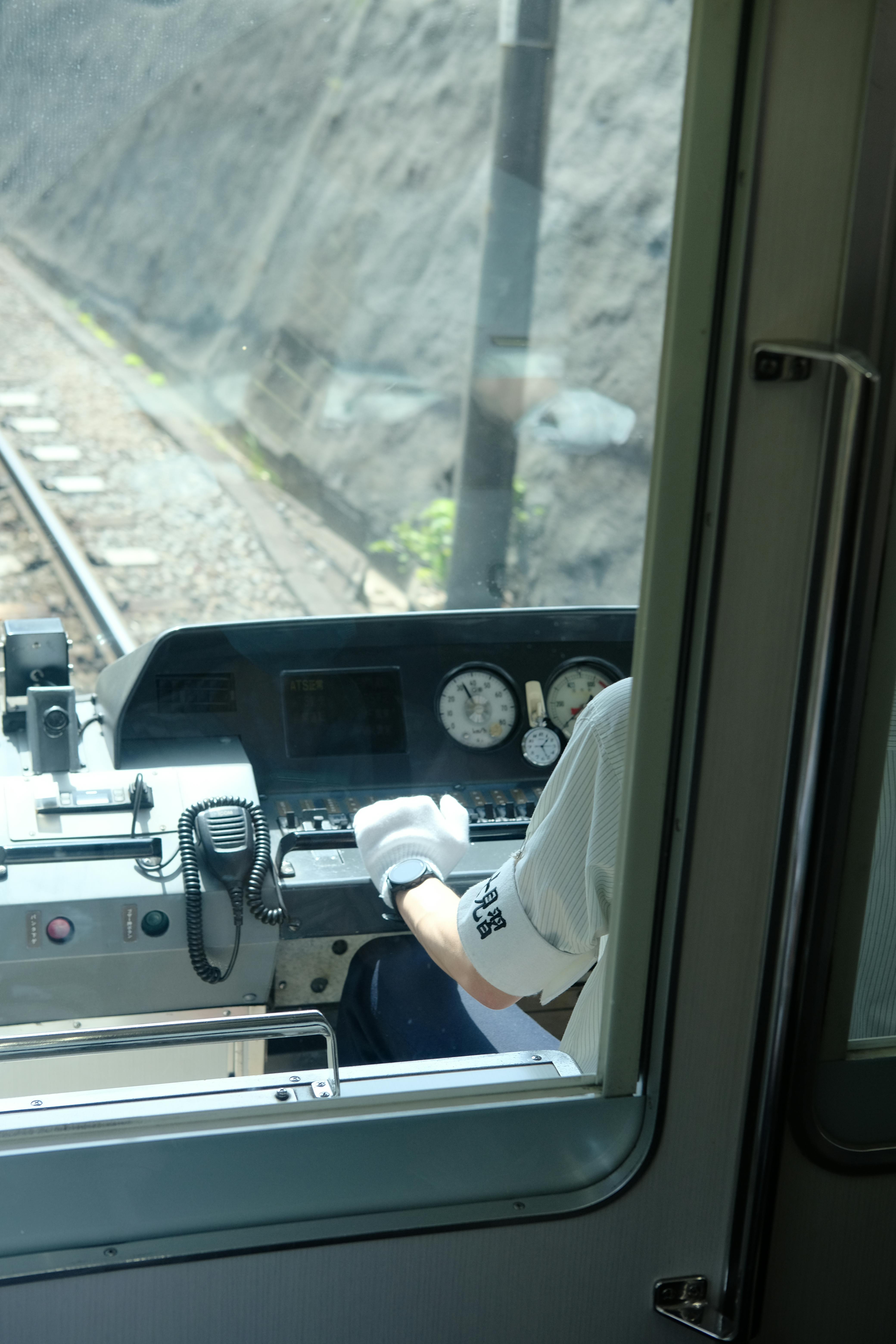 Rear view of a train conductor operating the controls in a cabin, focusing on the dashboard and controls.