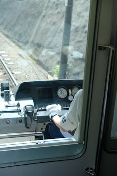 Rear view of a train conductor operating the controls in a cabin, focusing on the dashboard and controls.