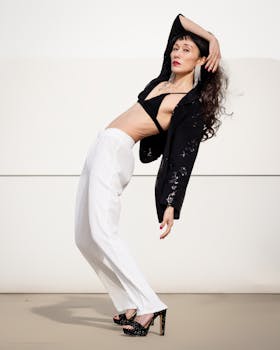 A stylish woman striking a dramatic, leaning pose showcasing modern fashion against a minimalist background.