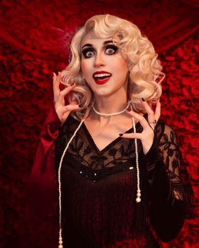 A dramatic vintage portrait of a woman with blonde curls and pearl necklace against a red floral backdrop.