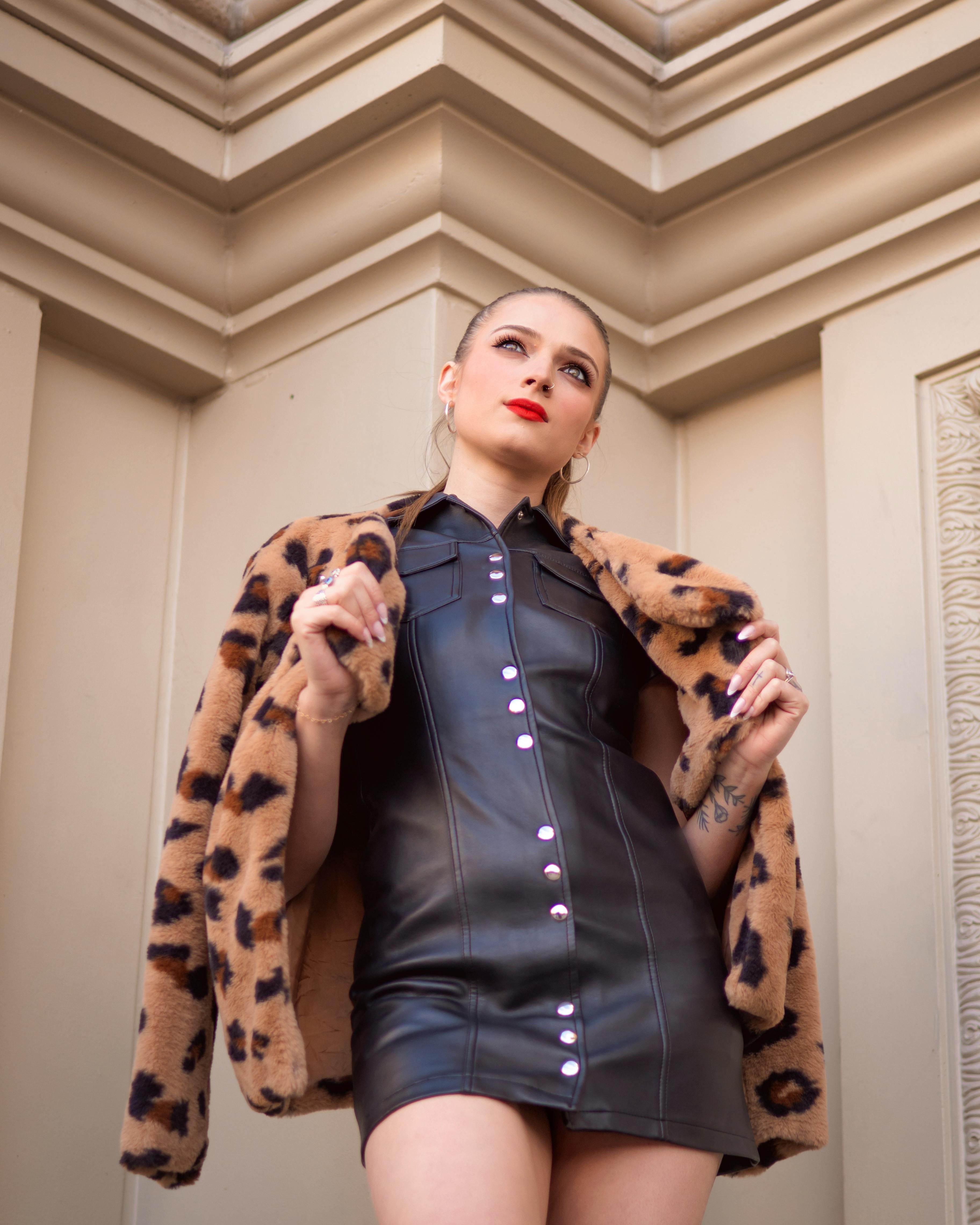 Fashionable woman in a leather dress with leopard coat striking a confident pose.