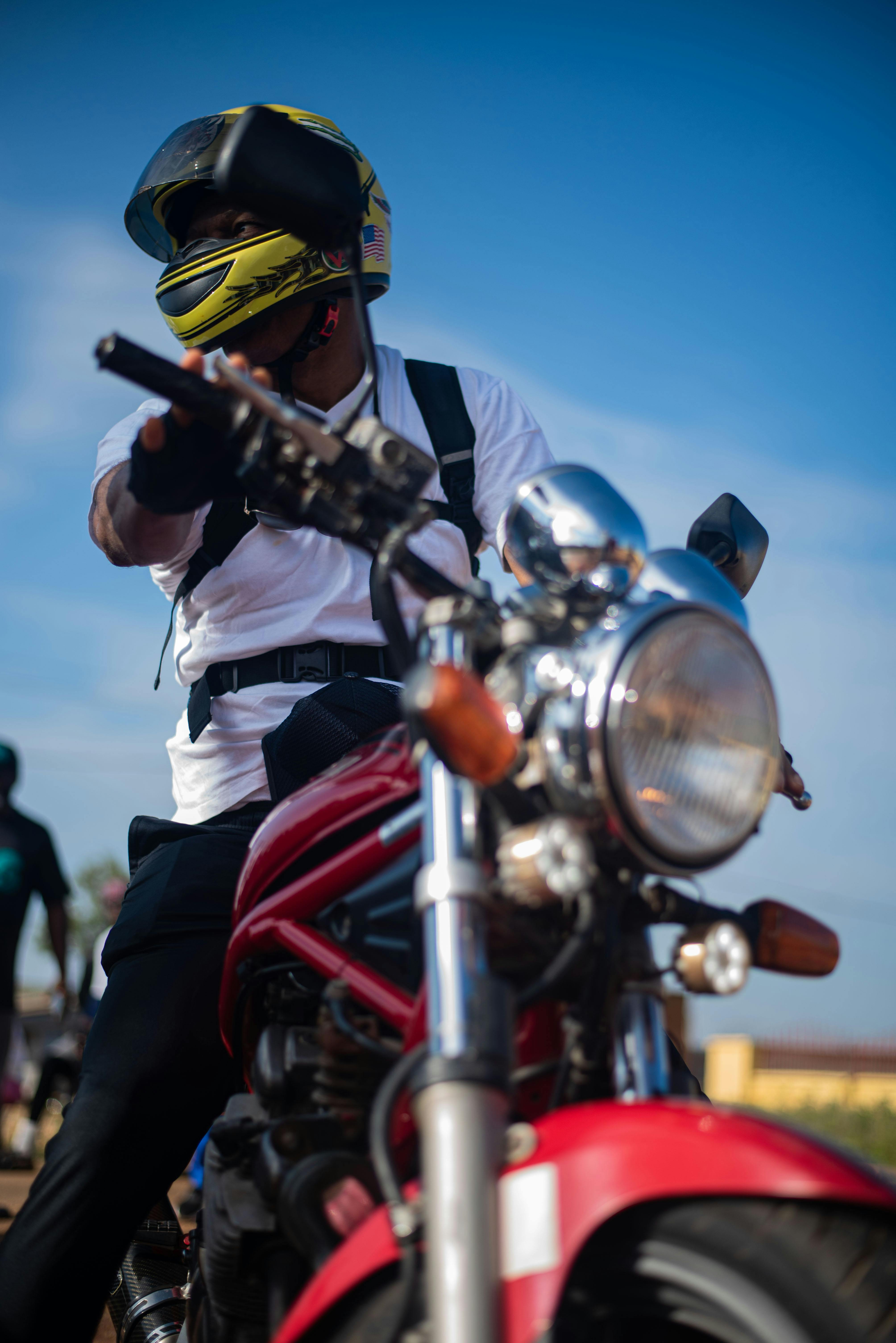 Person wearing helmet rides red motorcycle in sunny outdoor setting, showcasing action and adventure.