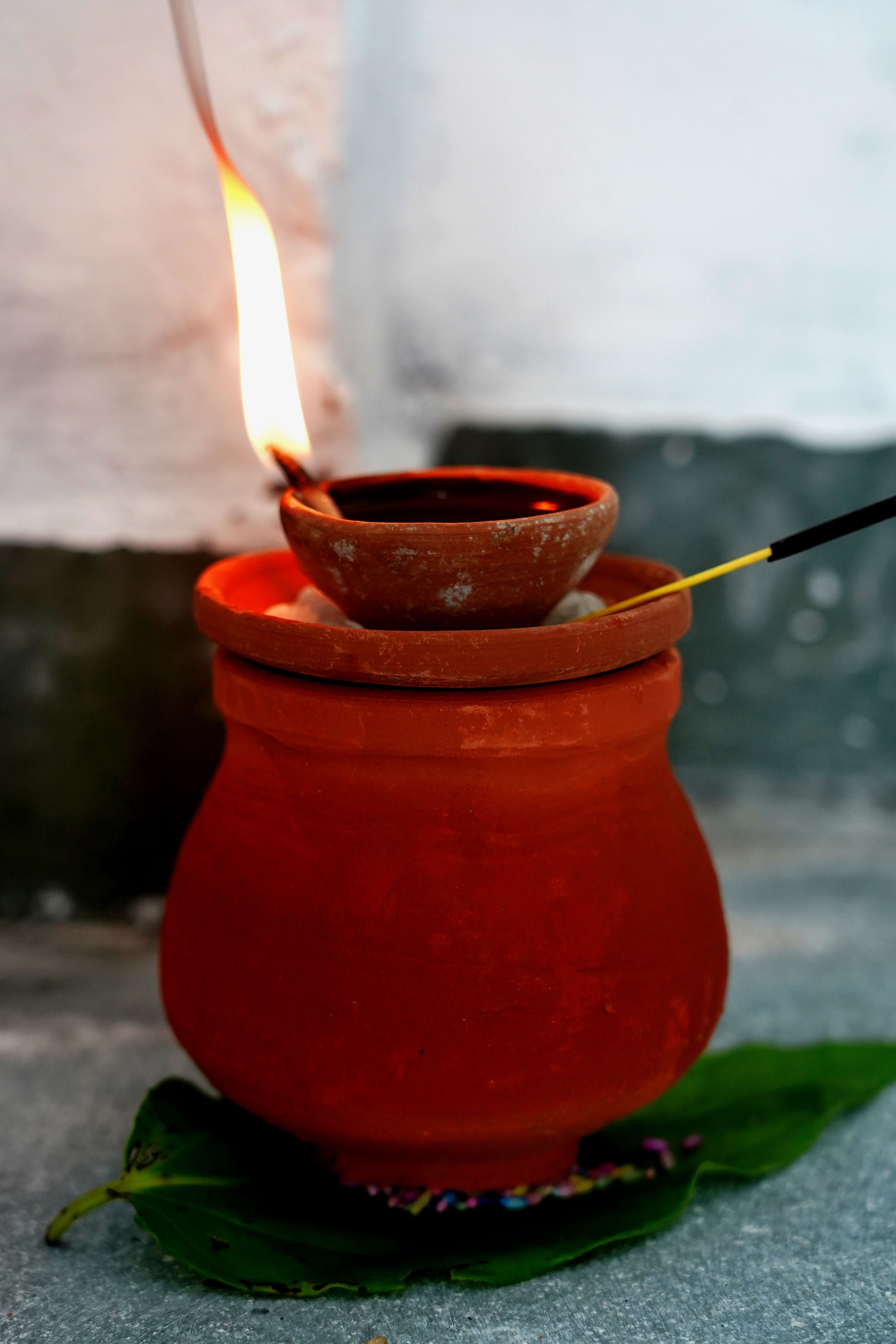 A close-up of a lit earthen diya with incense stick in an indoor setting, symbolizing cultural rituals.