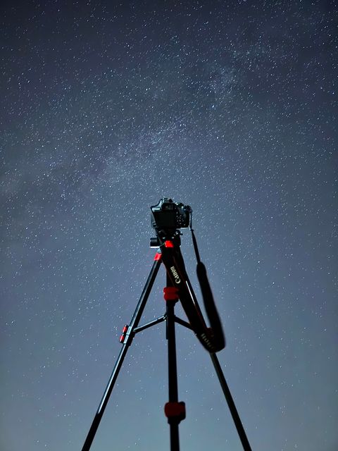 A camera on a tripod pointed up into a deep blue starry sky