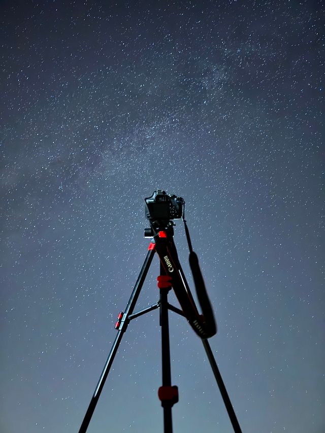 A camera on a tripod pointed up into a deep blue starry sky