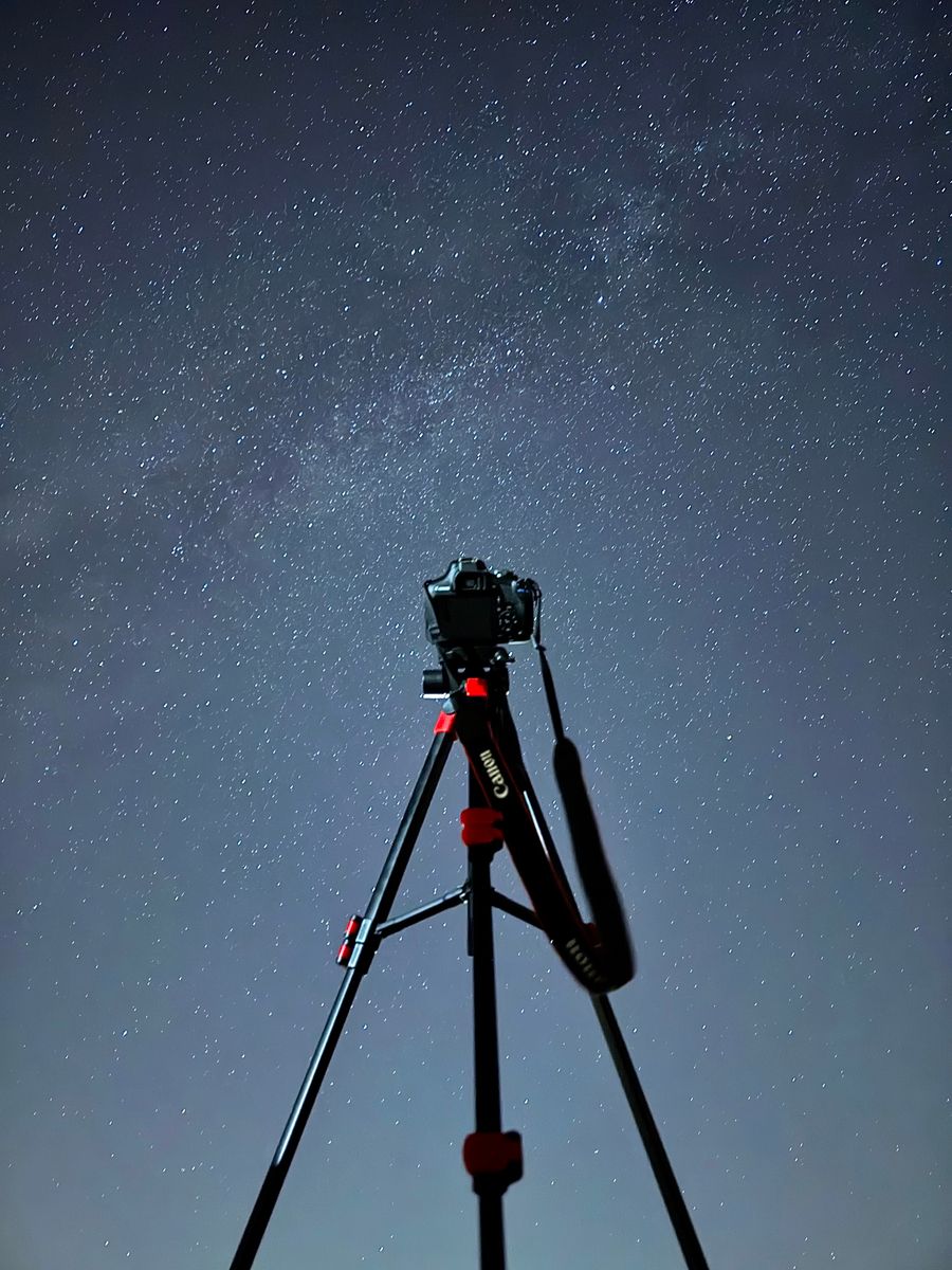 A camera on a tripod pointed up into a deep blue starry sky