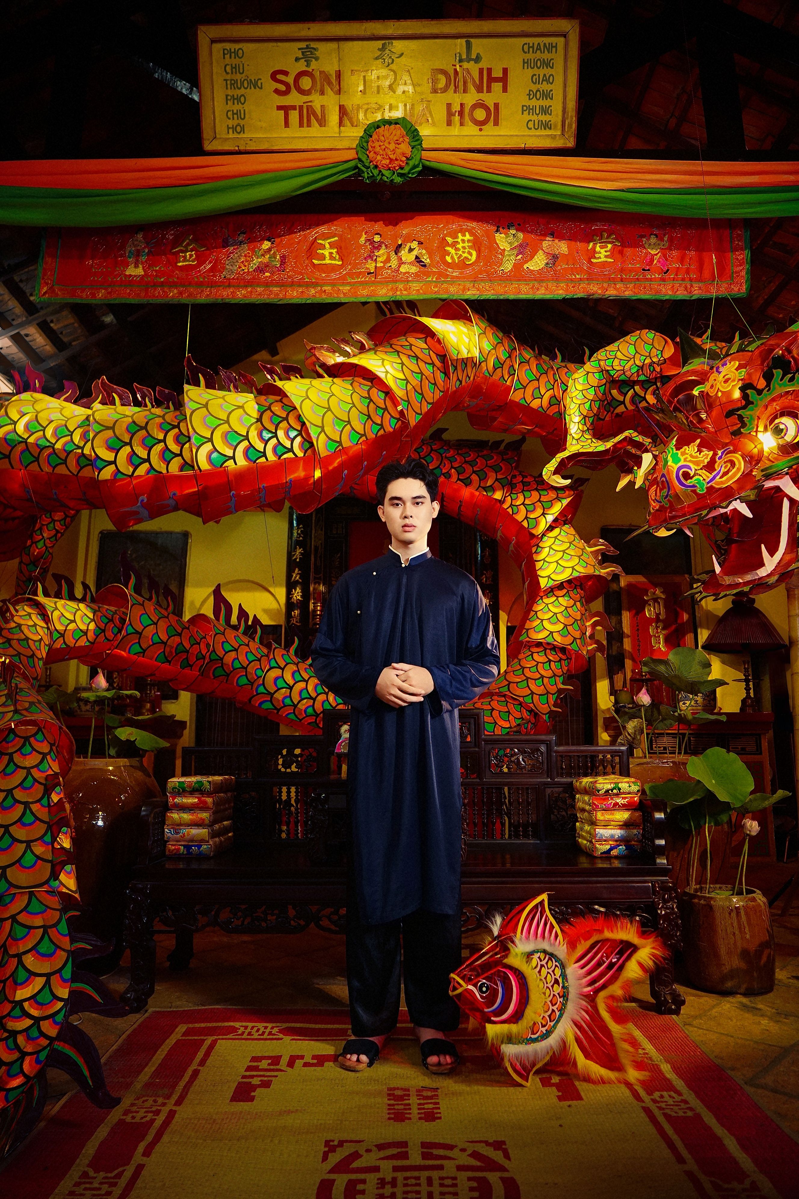 A Vietnamese man in traditional attire at a temple with dragon decorations.