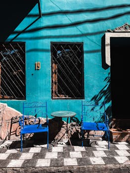 Vibrant blue chairs and table against a teal wall in a sunny outdoor street setting.