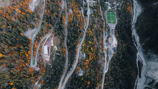 Stunning aerial view of winding mountain roads surrounded by autumn foliage and a football field in Anniviers, Switzerland.