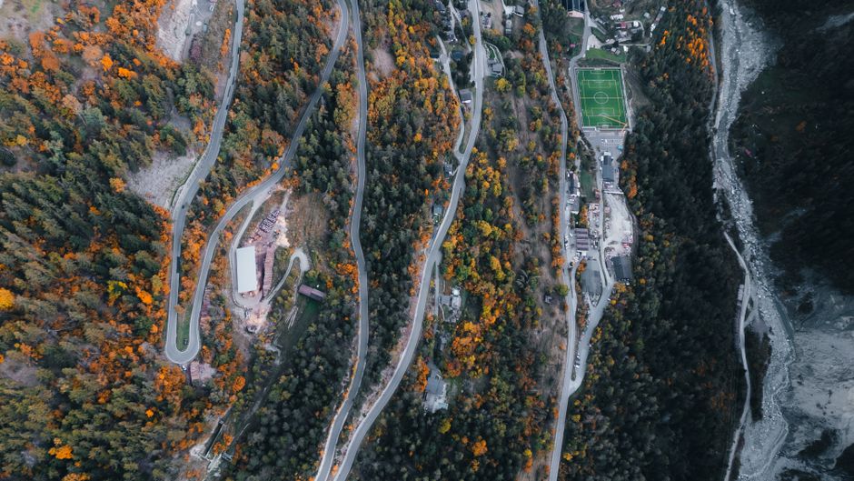 Stunning aerial view of winding mountain roads surrounded by autumn foliage and a football field in Anniviers, Switzerland.