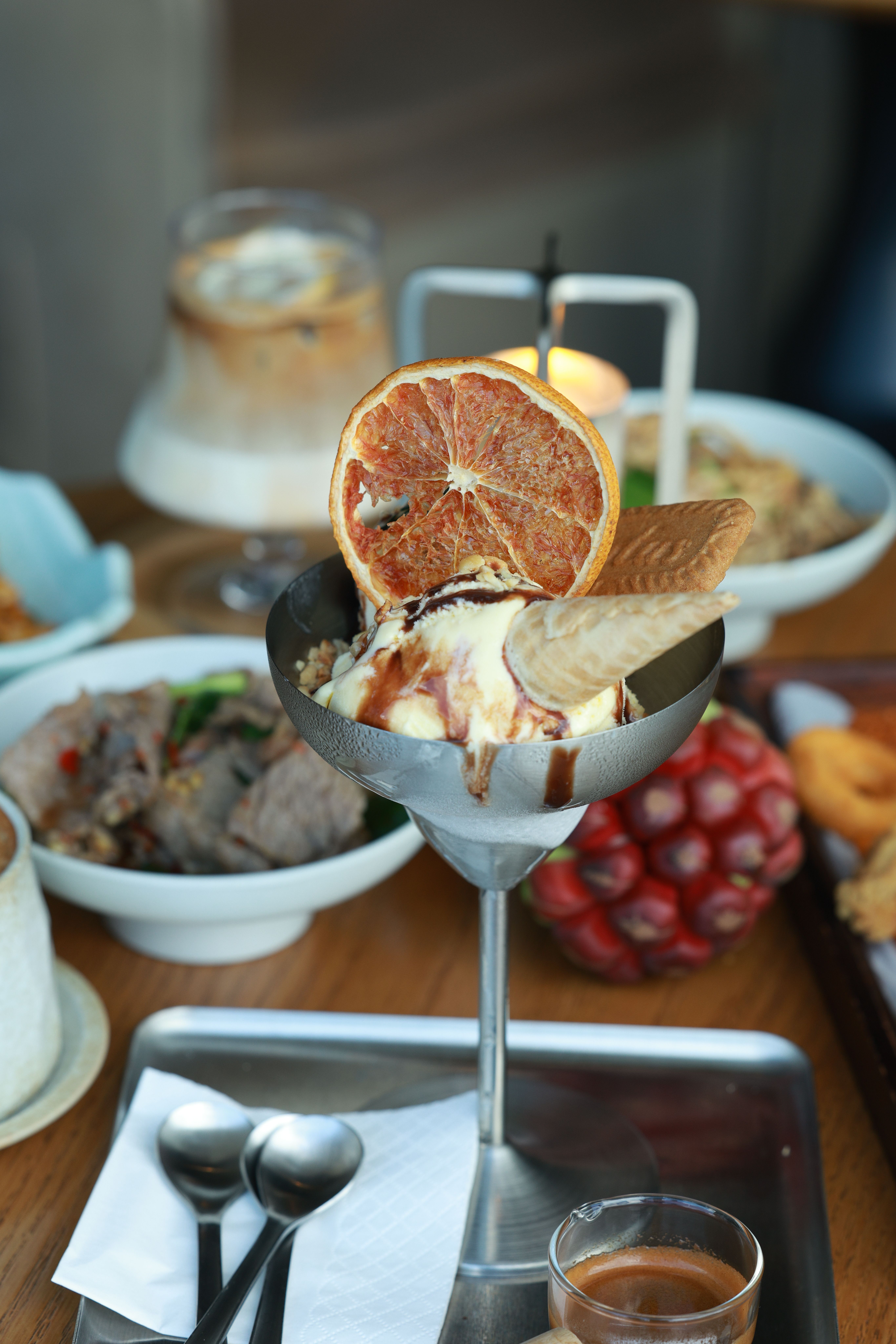 Elegant dessert with dried orange slice, creamy ice cream in cocktail glass, and dining table setup.