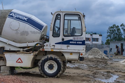 Close-up of a concrete mixer truck at a construction site under cloudy skies.