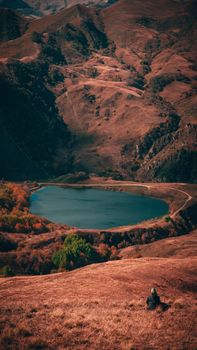 Dramatic autumn landscape with a lone traveler by a tranquil lake in the mountains.