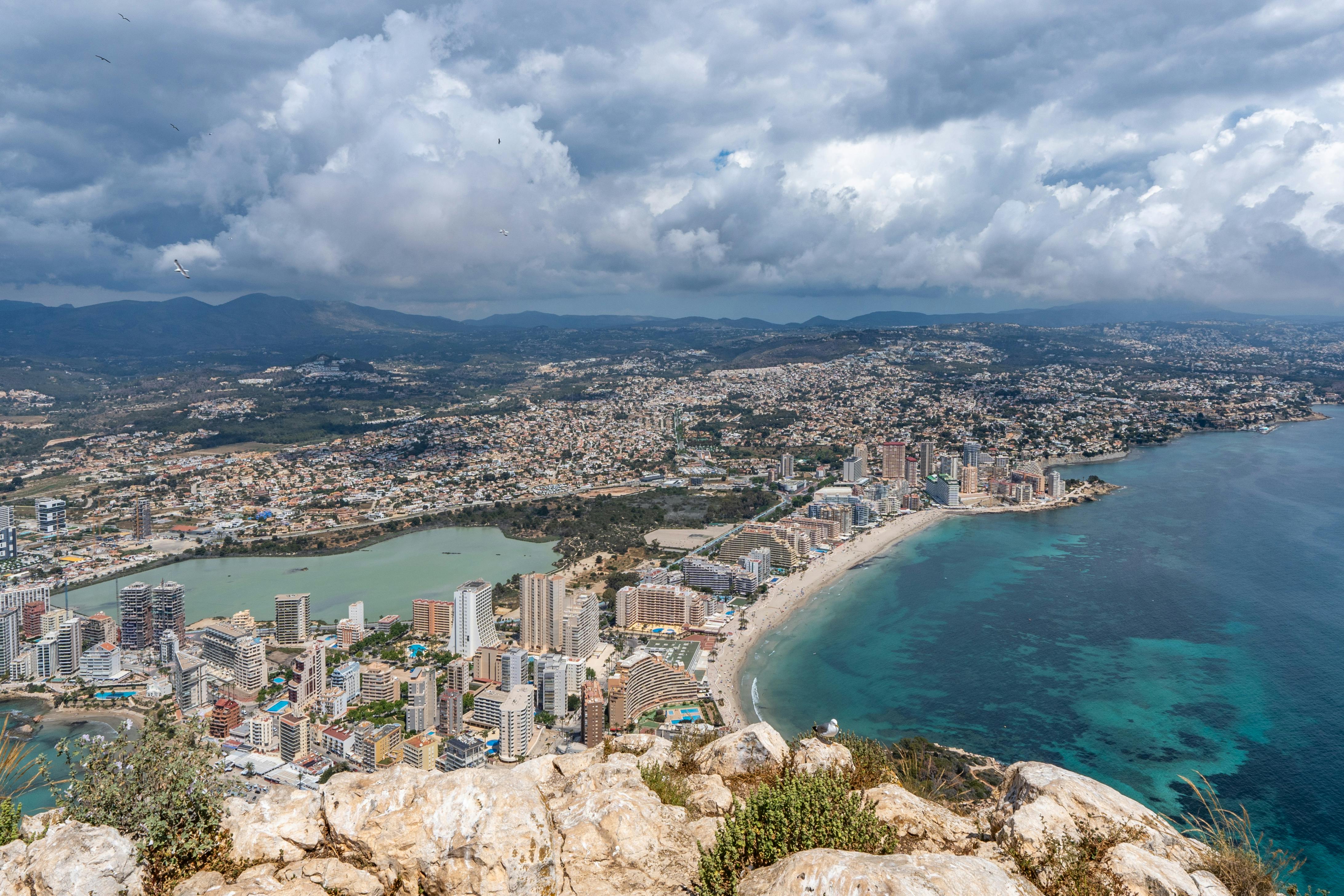 Stunning aerial view of Calpe's coastline and cityscape under dramatic clouds.