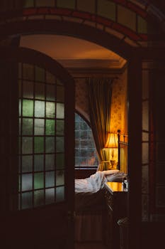 Warm and inviting Victorian bedroom featuring stained glass and a glowing bedside lamp.