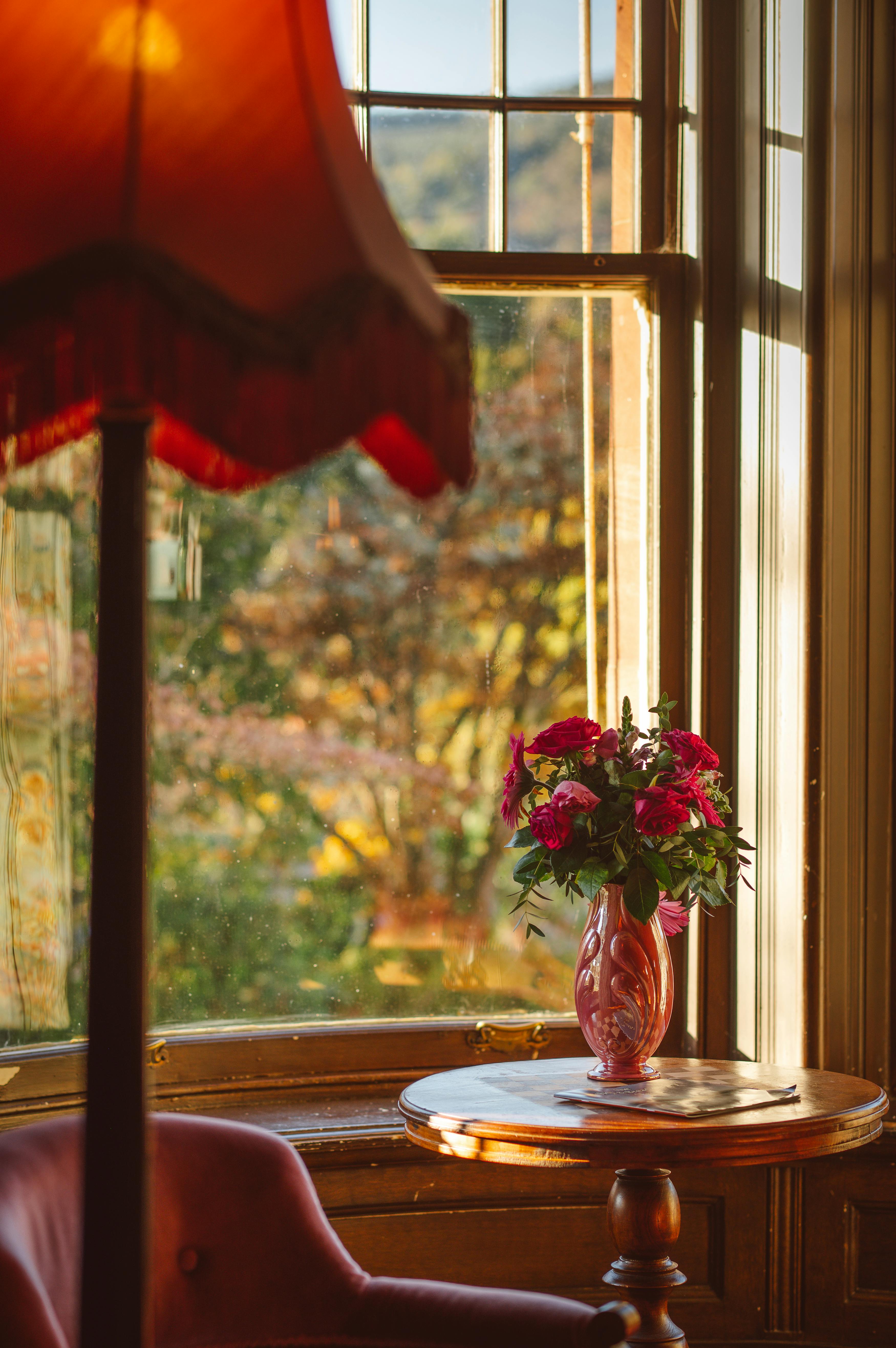 A cozy Victorian room featuring a red lampshade and a pink vase with flowers by the window.