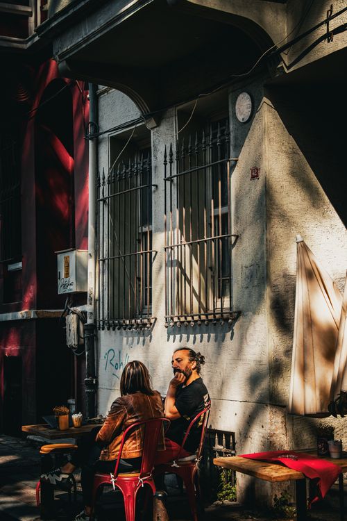 Free Two adults chatting at an outdoor café table with artistic shadows in urban setting. Stock Photo