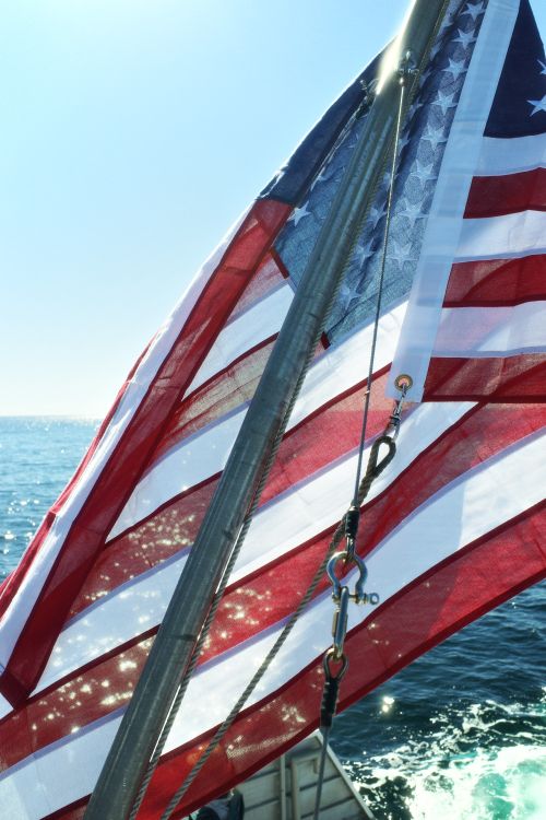 Free Close-up of a waving American flag on a boat sailing on the open ocean under a clear blue sky. Stock Photo